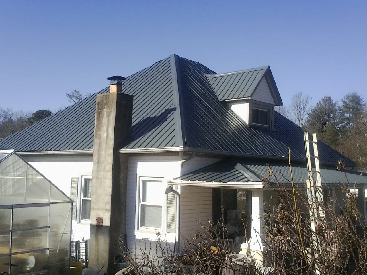 Dark blue standing seam metal roof on a white farmhouse with dormer — Slate & Tile Roof Repair by Roofing Brothers in Morrisonville
