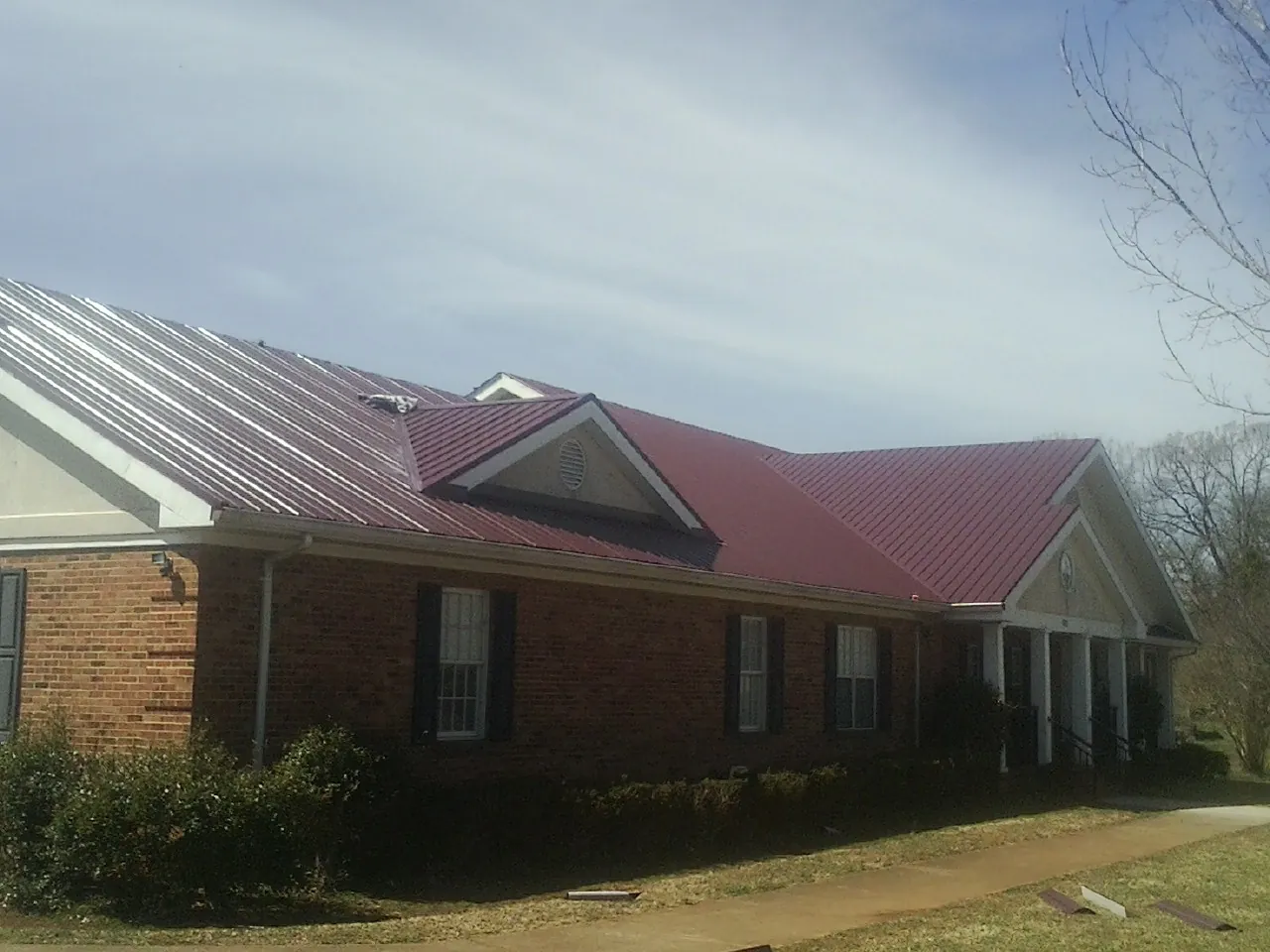 Red metal roof with gabled entries on a long brick building, from a Hail Damage Roof Repair job in Morrisonville