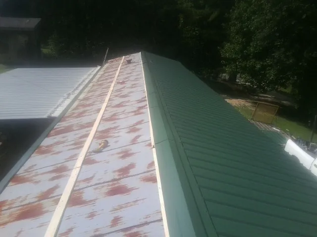 Old rusted panels beside newly installed green metal roofing — Wind Damage Roof Repair by Roofing Brothers in Morrisonville