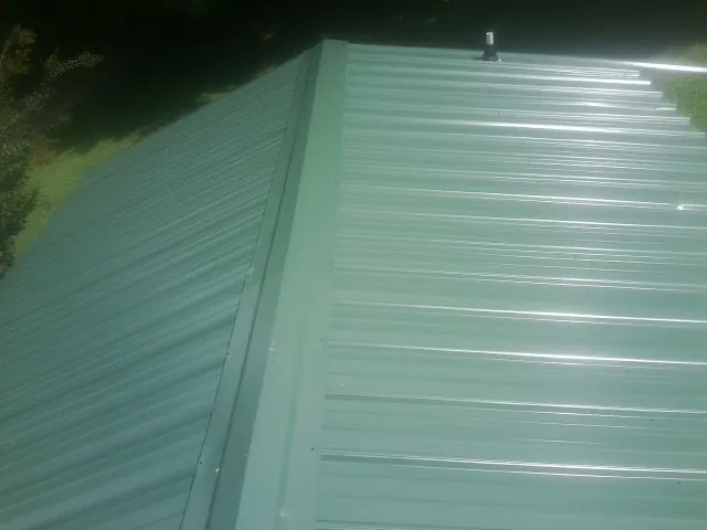 New green metal panels meeting at the ridge of a roof — Flat Roof Repair work by our crew in Morrisonville