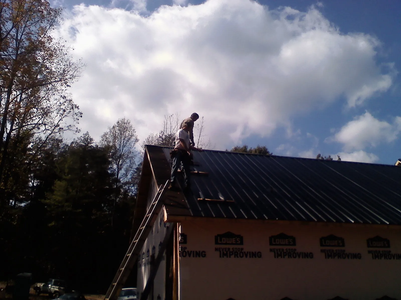Roofer fastening dark metal panels high against a cloudy sky, from a Roof Inspection job in Morrisonville
