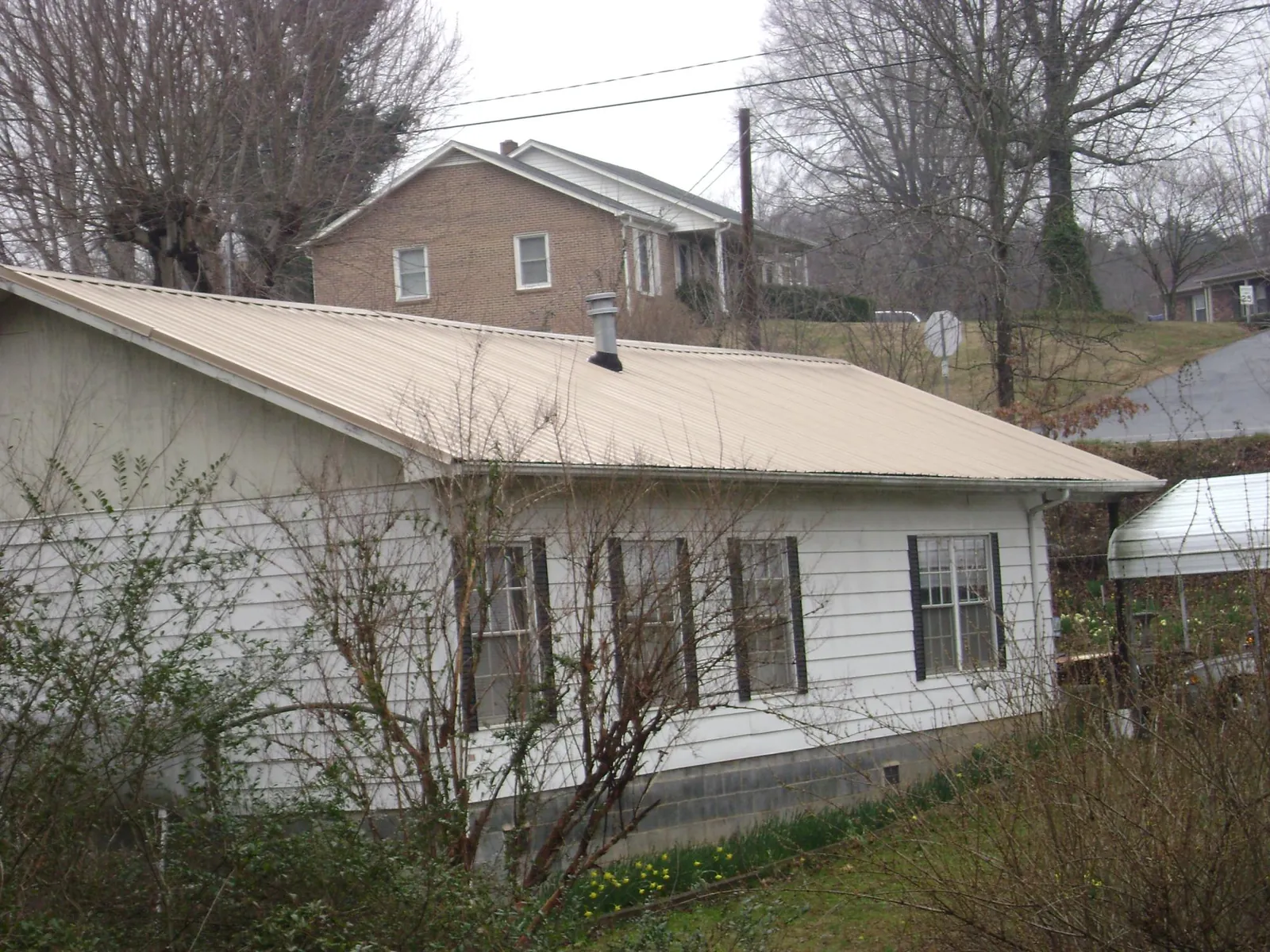 Tan metal roof on a white sided house set into a hillside — Commercial Roofing by Roofing Brothers in Morrisonville