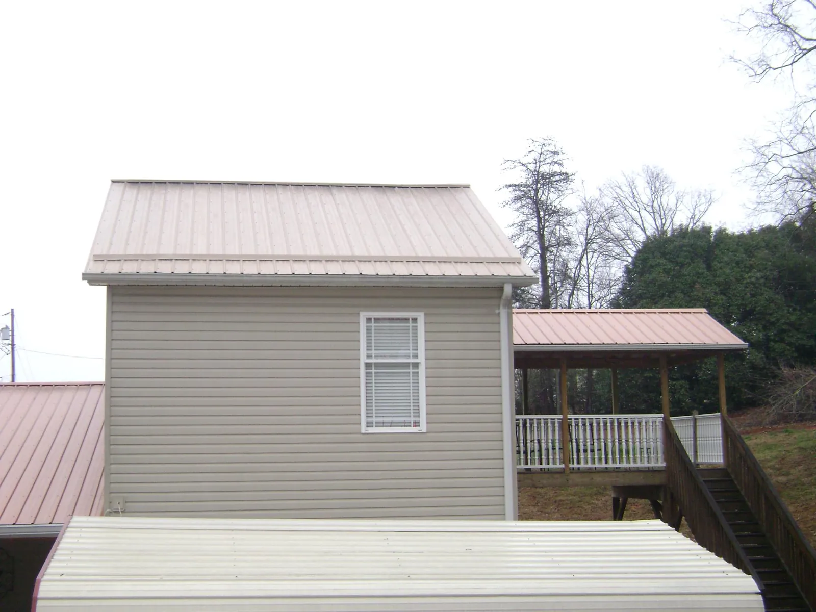 Tan metal roofs on a two story addition and attached porch, from a Roof Replacement job in Morrisonville
